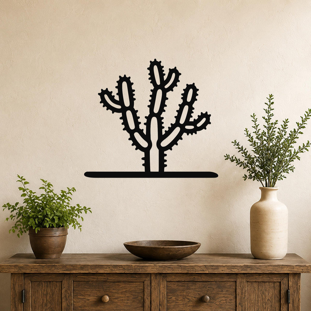 Black metal cholla cactus wall art with spiny branch cutouts, mounted on a beige wall above a wooden console table with potted plants.