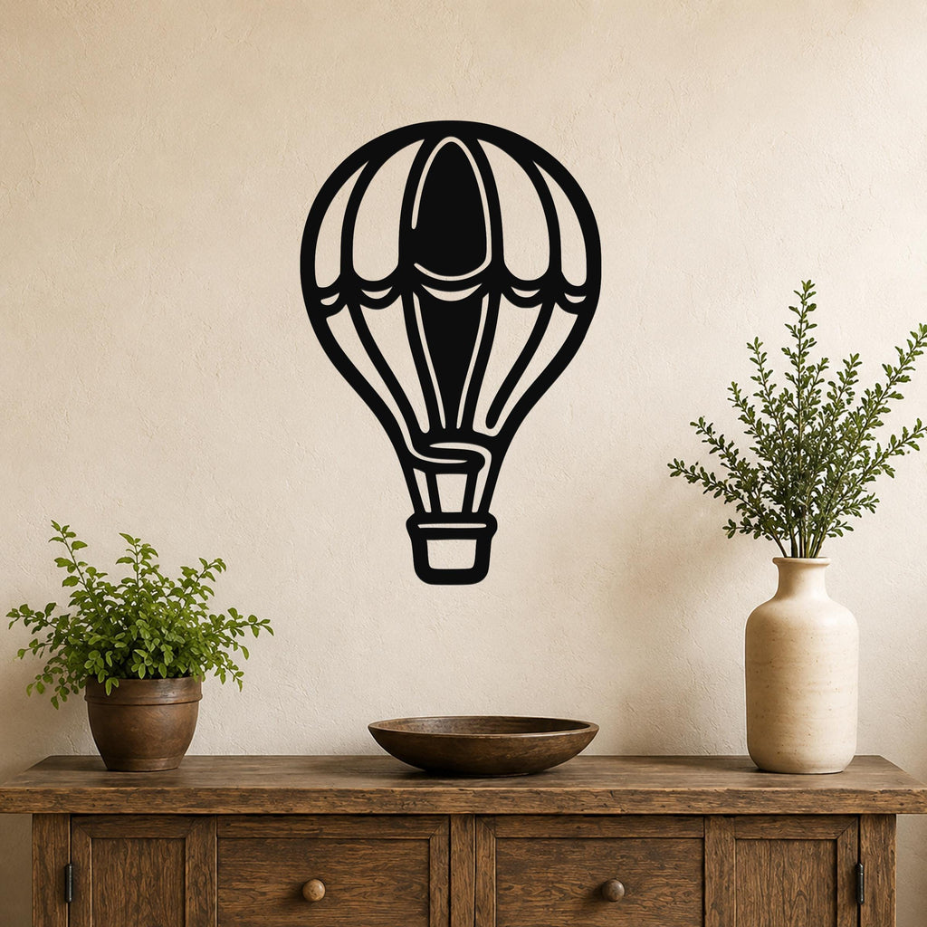 Black metal hot air balloon wall art with internal cutout details, mounted on a beige wall above a wooden console table with potted plants.