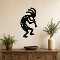 Black metal Kokopelli wall art silhouette with internal cutout details, mounted on a beige wall above a wooden console table with potted plants.