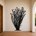 Black metal ocotillo wall art with branching stems and flower cutouts, mounted on a beige wall in a covered entryway with terracotta tile flooring.