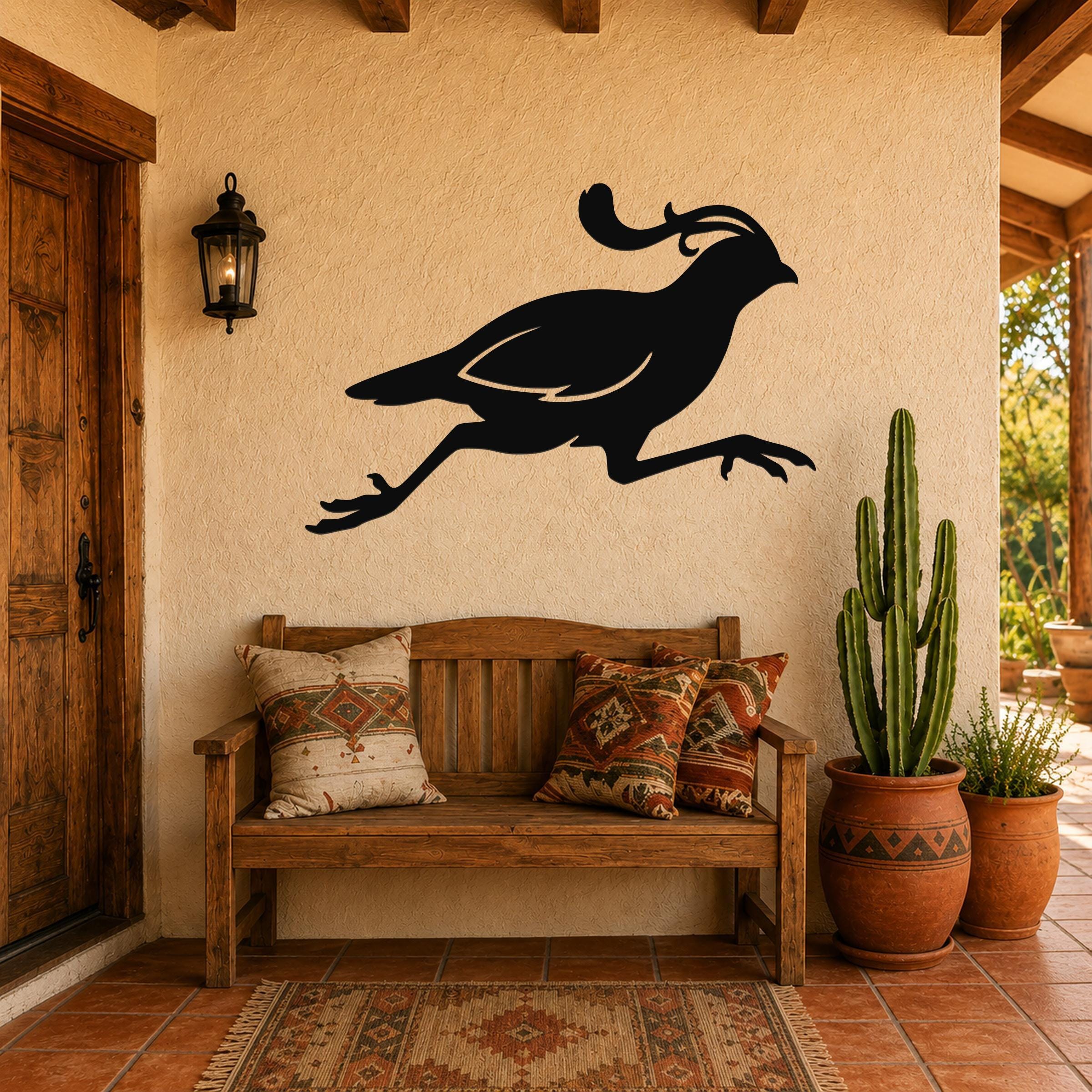 Black metal quail wall art with motion-line cutouts, mounted above a wooden bench on a stucco patio wall.