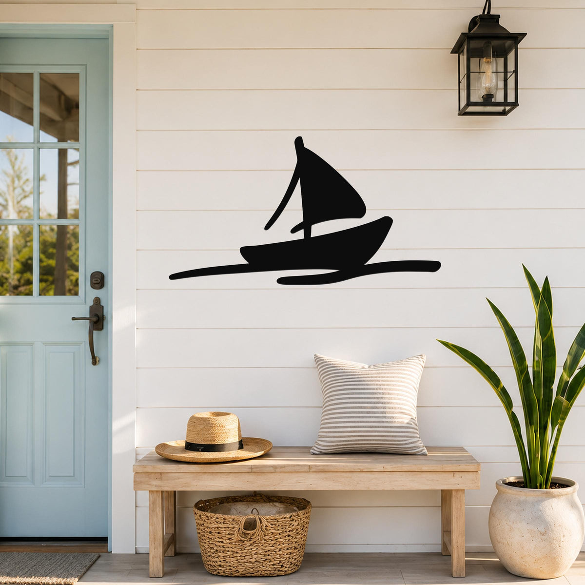 Black metal sailboat wall art with a silhouette design, mounted on a white shiplap wall above a wooden bench in a coastal entryway.