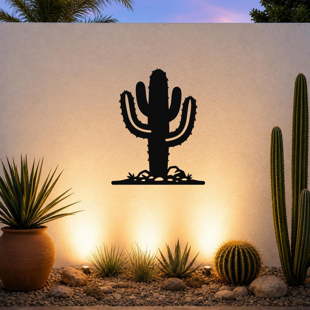 Black metal Saguaro cactus wall art with spines and base cutouts, mounted on a textured outdoor wall above a desert garden with potted plants and ground lights.