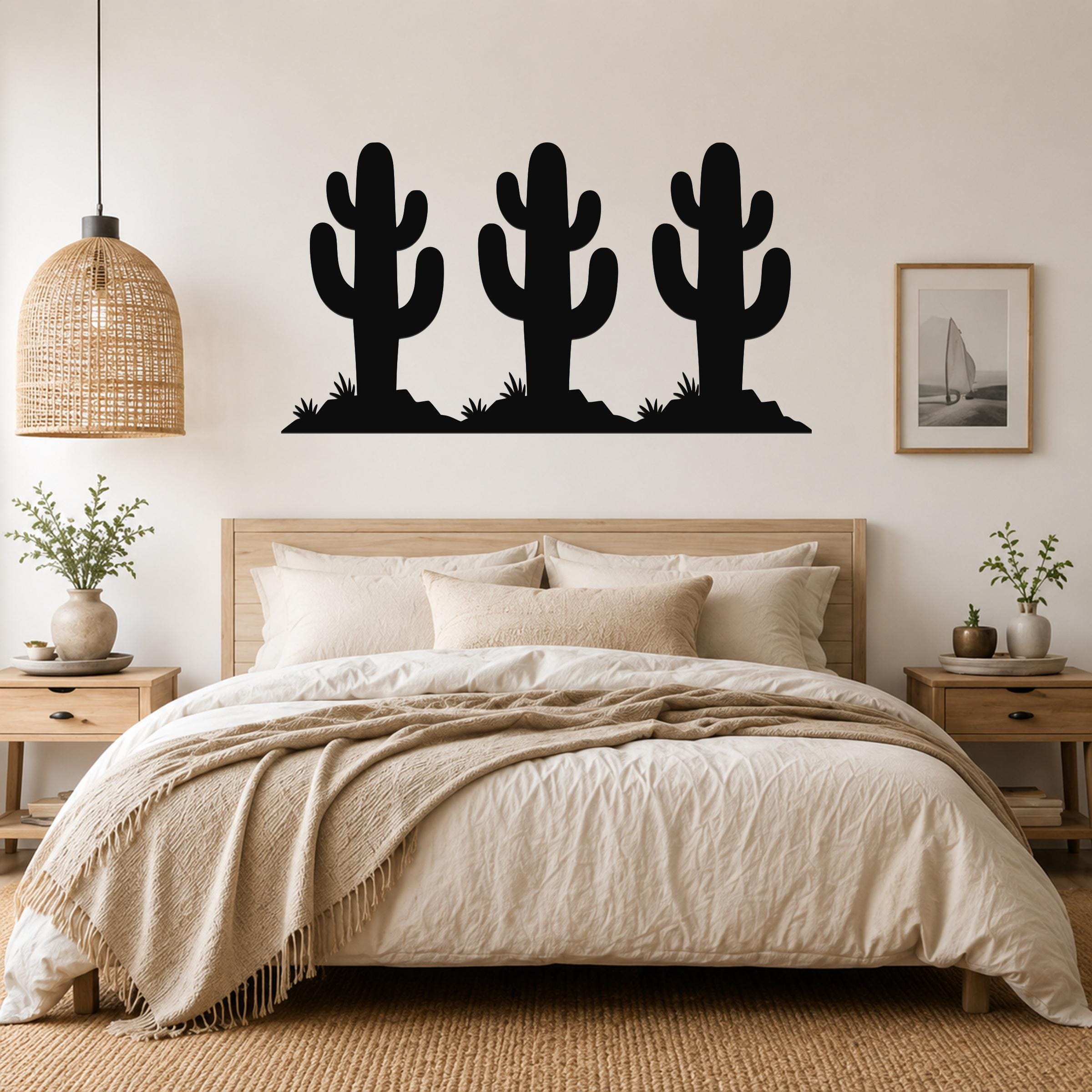 Black metal wall art featuring a silhouette of three saguaro cacti with spines and small plants, mounted above a wooden bed in a bedroom.