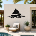 Black metal sailboat wall art with wave cutouts, mounted on an outdoor patio wall above a lounge chair.