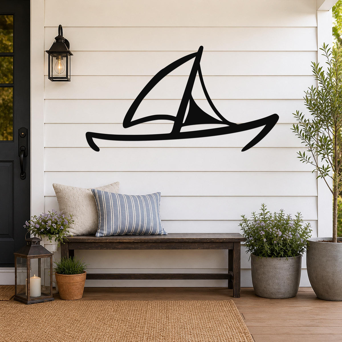 Black metal sailboat wall art with a silhouette design, mounted on a white shiplap wall above a wooden bench in a coastal porch setting.
