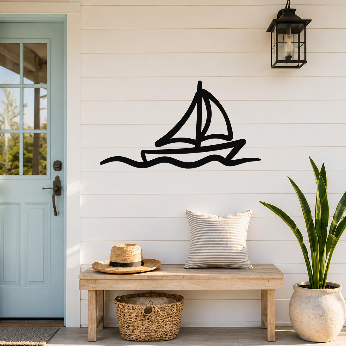 Black metal sailboat wall art with wavy line cutout, mounted on a white shiplap wall above a wooden bench in a coastal entryway.