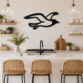 Black metal seagull wall art with flowing wing cutouts, mounted above a kitchen counter in a coastal-style kitchen.