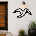 Black metal seagull wall art with flowing motion lines, mounted on a white exterior wall above a potted succulent and near a wooden front door.