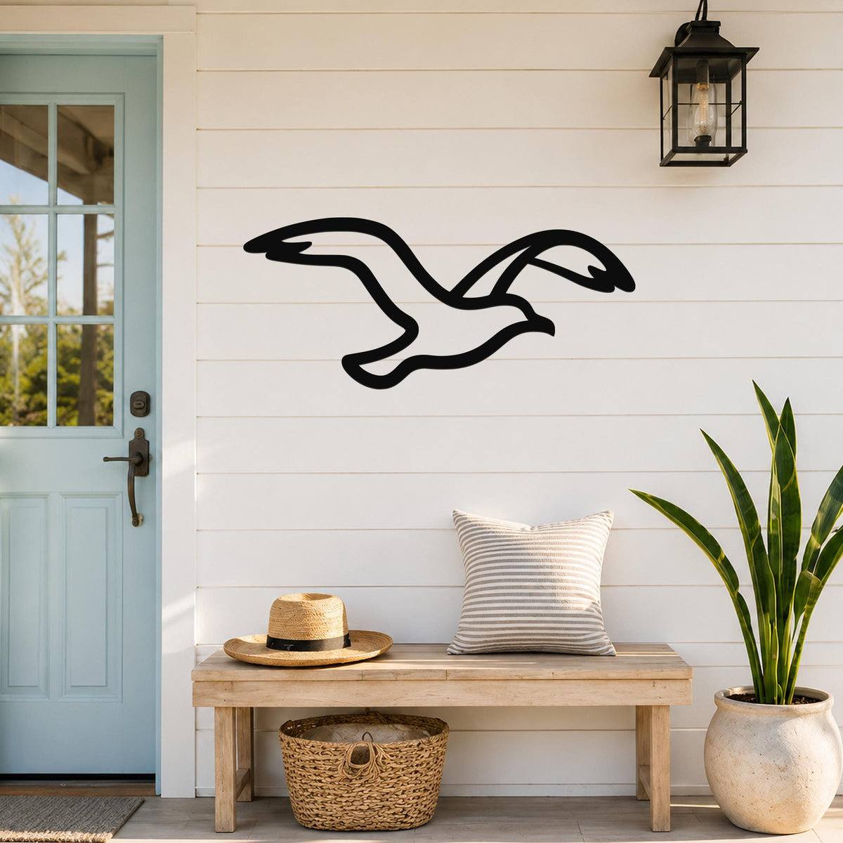 Black metal seagull wall art with motion-line cutouts, mounted on a white shiplap wall above a wooden bench in a coastal entryway.