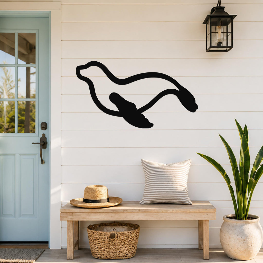 Black metal sea lion wall art with a flowing silhouette, mounted on a white shiplap wall above a wooden bench in a coastal entryway.