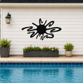 Black metal sea urchin wall art with spiky cutout design, mounted on a white horizontal siding wall above a poolside planter.