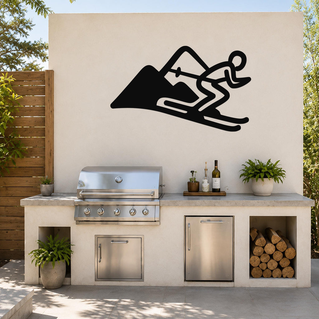 Black metal skier and mountain wall art silhouette mounted above a stainless steel outdoor grill on a patio wall.