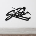 Black metal wall art featuring a skier silhouette with mountain peaks and the word "SKI" in cursive, mounted on a white wall above a wooden surface.