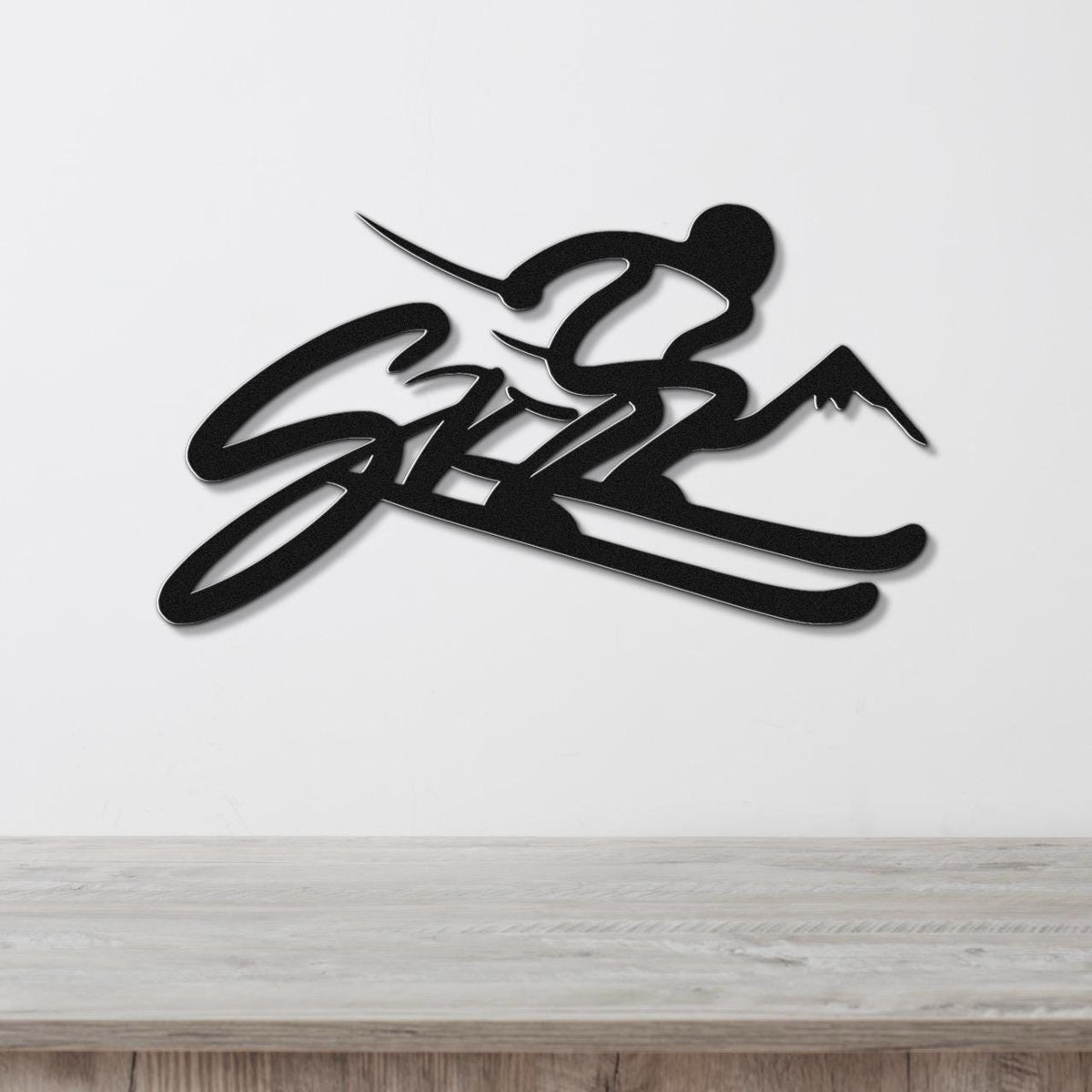 Black metal wall art featuring a skier silhouette with mountain peaks and the word "SKI" in cursive, mounted on a white wall above a wooden surface.
