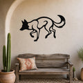 Black metal coyote wall art with a bold silhouette design, mounted on a textured beige wall above a rustic wooden bench in a patio setting.