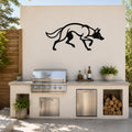 Black metal coyote wall art with motion-line cutouts, mounted on an outdoor kitchen wall above a stainless steel grill and counter.