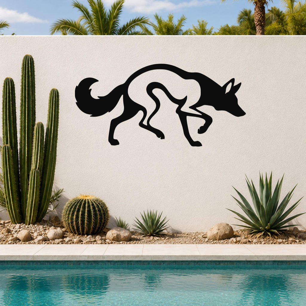 Black metal coyote wall art with a silhouette cutout design, mounted on an outdoor wall above a pool with cacti and palm trees in the background.