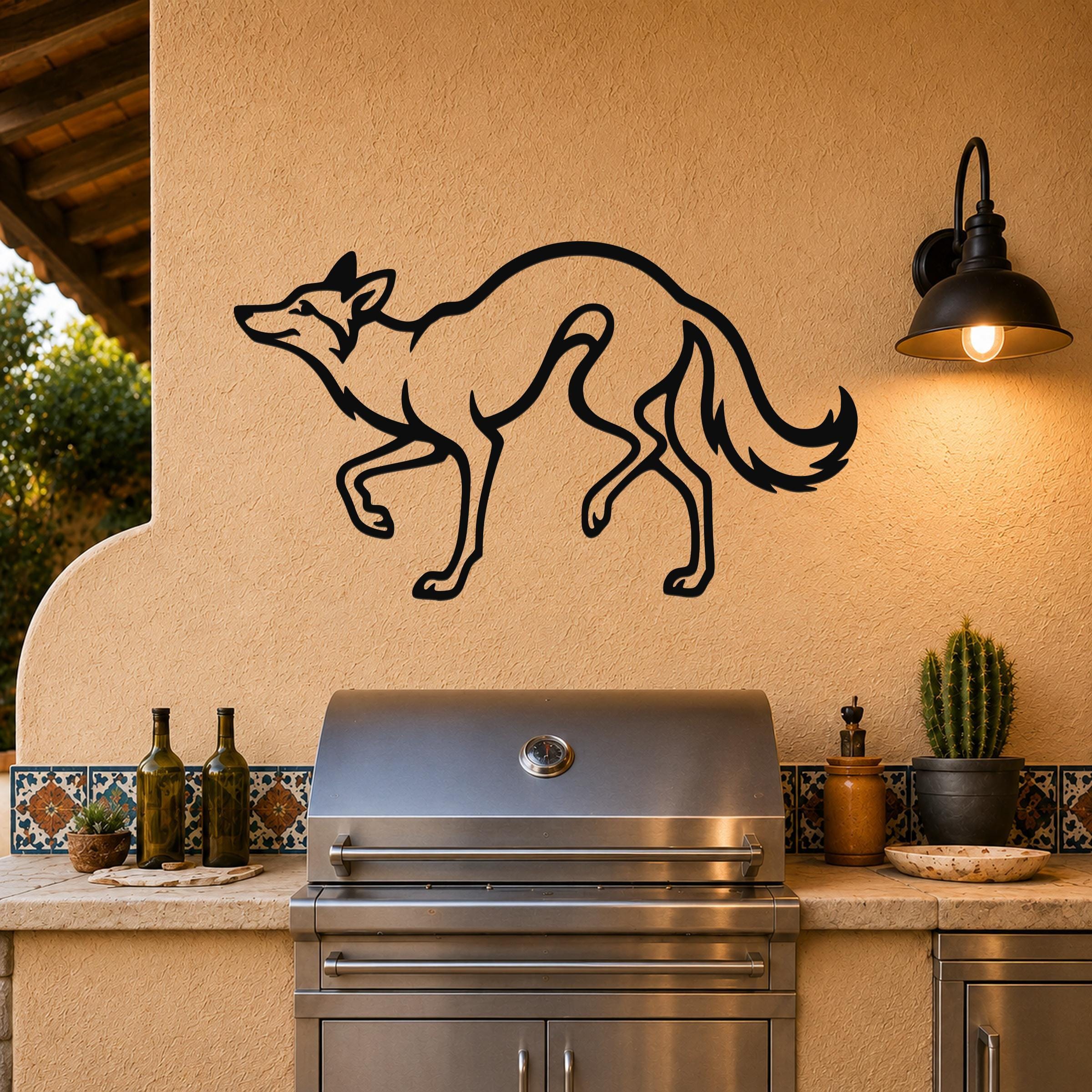 Black metal coyote wall art with a silhouette cutout design, mounted on an outdoor patio wall above a stainless steel grill.