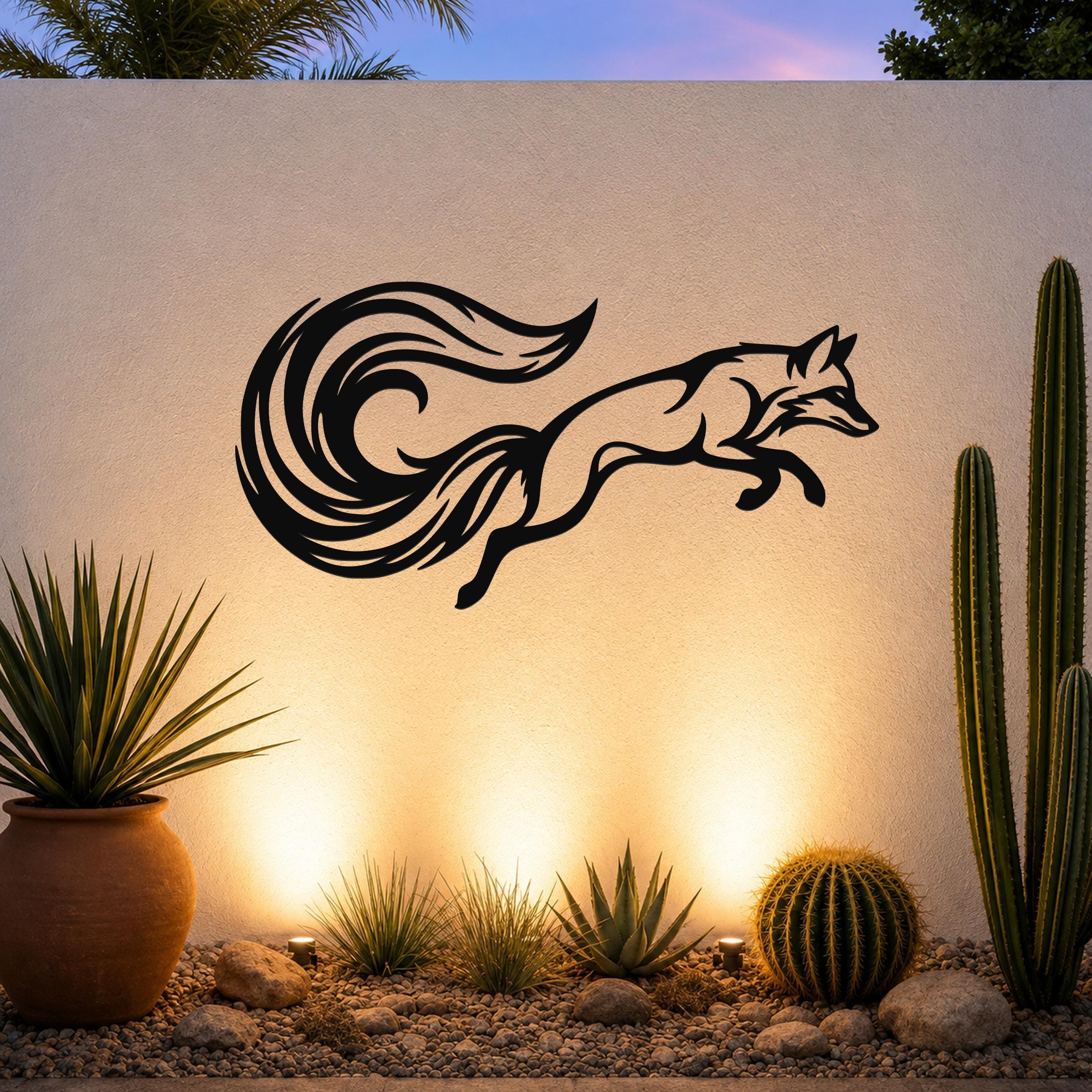 Black metal fox wall art with flowing tail cutout, mounted on an outdoor wall above a desert garden with cacti and warm uplighting.