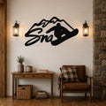 Black metal wall art featuring a snowboarder silhouette and mountain outline, mounted above a wooden console table in a living room with shiplap walls and lanterns.