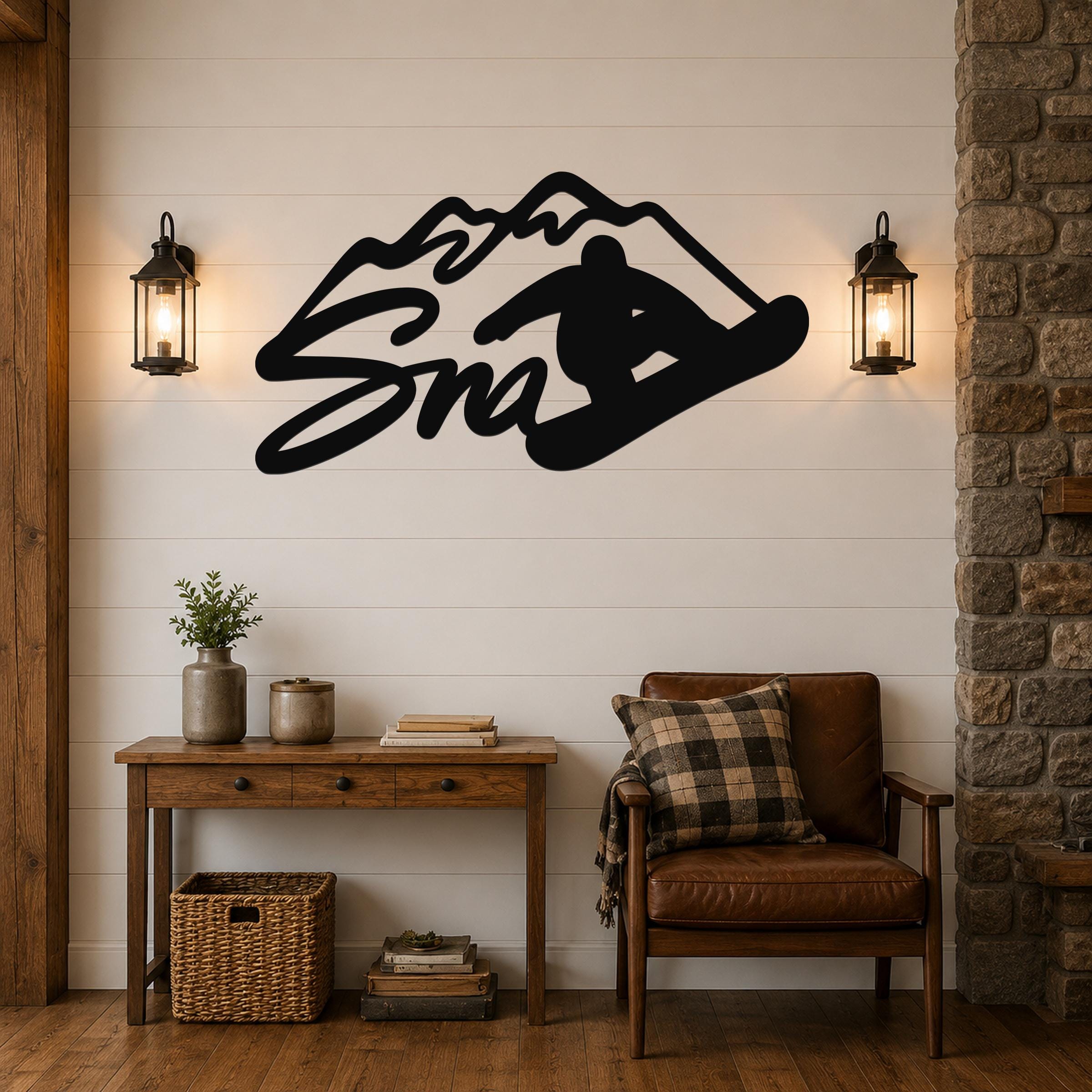 Black metal wall art featuring a snowboarder silhouette and mountain outline, mounted above a wooden console table in a living room with shiplap walls and lanterns.
