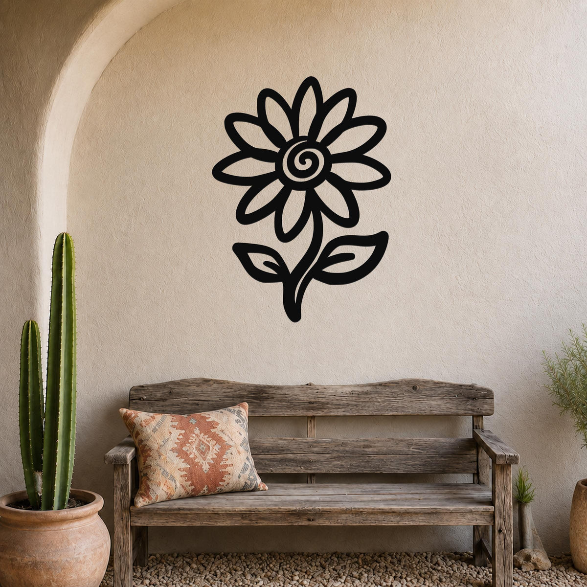 Black metal sunflower wall art with a spiral center and leaf cutouts, mounted on a textured beige wall above a rustic wooden bench in a patio setting.