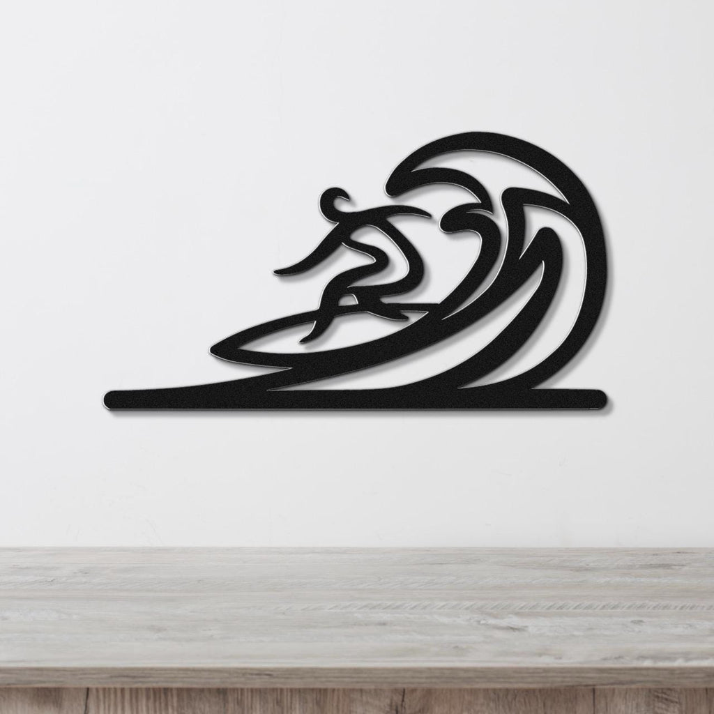 Black metal wall art featuring a surfer silhouette riding a flowing wave, mounted on a white wall above a wooden surface.