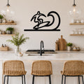 Black metal surfer wall art with a wave silhouette, mounted above a kitchen counter in a bright, modern kitchen.