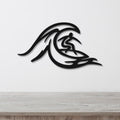 Black metal wall art featuring a surfer silhouette riding a wave, mounted on a white wall above a wooden surface.