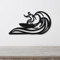 Black metal wall art featuring a surfer silhouette riding a wave, mounted on a white wall above a wooden surface.