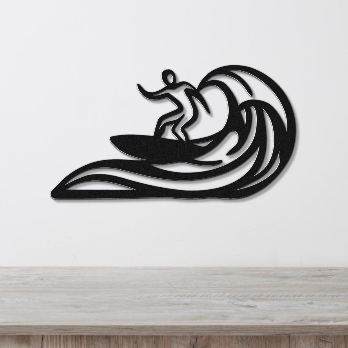 Black metal wall art featuring a surfer silhouette riding a wave, mounted on a white wall above a wooden surface.