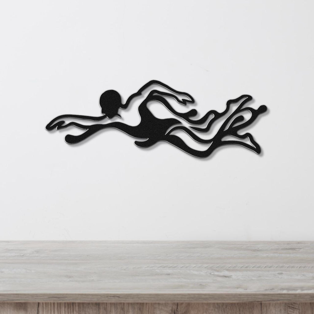 Black metal wall art of a swimmer in motion with flowing water cutouts, mounted on a white wall above a light wood surface.