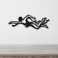 Black metal wall art of a swimmer in motion with flowing water cutouts, mounted on a white wall above a light wood surface.