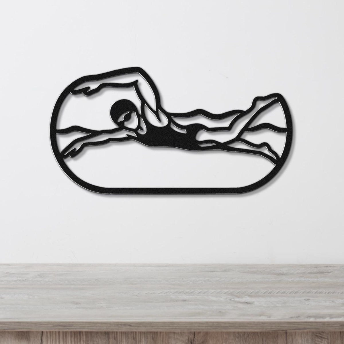 Black metal swimmer wall art with motion-line cutouts, mounted on a white wall above a light wood counter.
