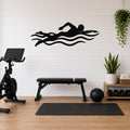 Black metal swimmer wall art with motion-line cutouts, mounted on a white shiplap wall above a workout bench in a home gym.
