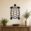 Black metal tortoise wall art with a cutout shell design, mounted on a beige wall above a wooden console table with potted plants.