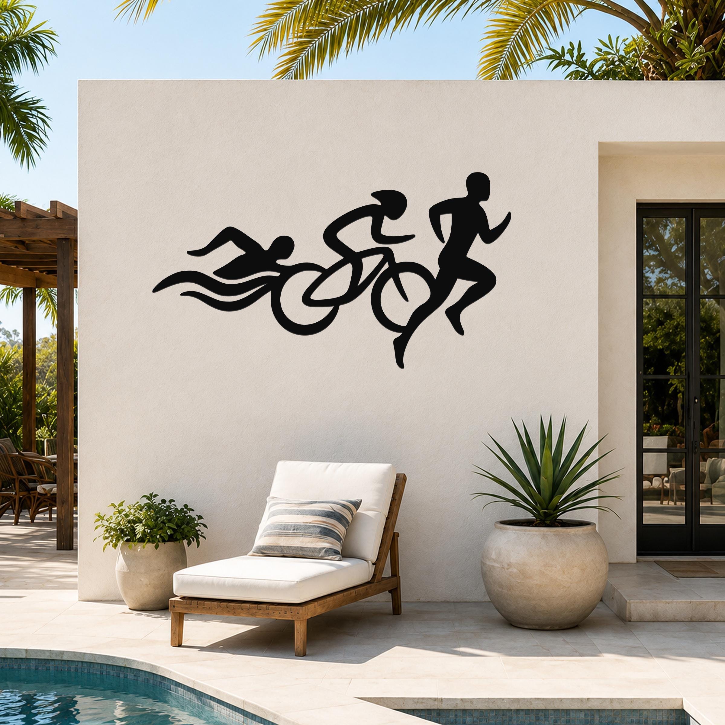 Black metal triathlon wall art with swim, bike, and run silhouettes, mounted on an outdoor patio wall above a lounge chair.