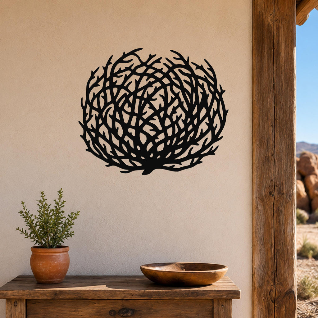 Black metal tumbleweed wall art with intricate branch cutouts, mounted on a beige wall above a wooden table in a southwestern-style outdoor entryway.