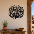 Black metal tumbleweed wall art with intricate branch cutouts, mounted on a beige wall above a wooden table in a southwestern-style outdoor entryway.