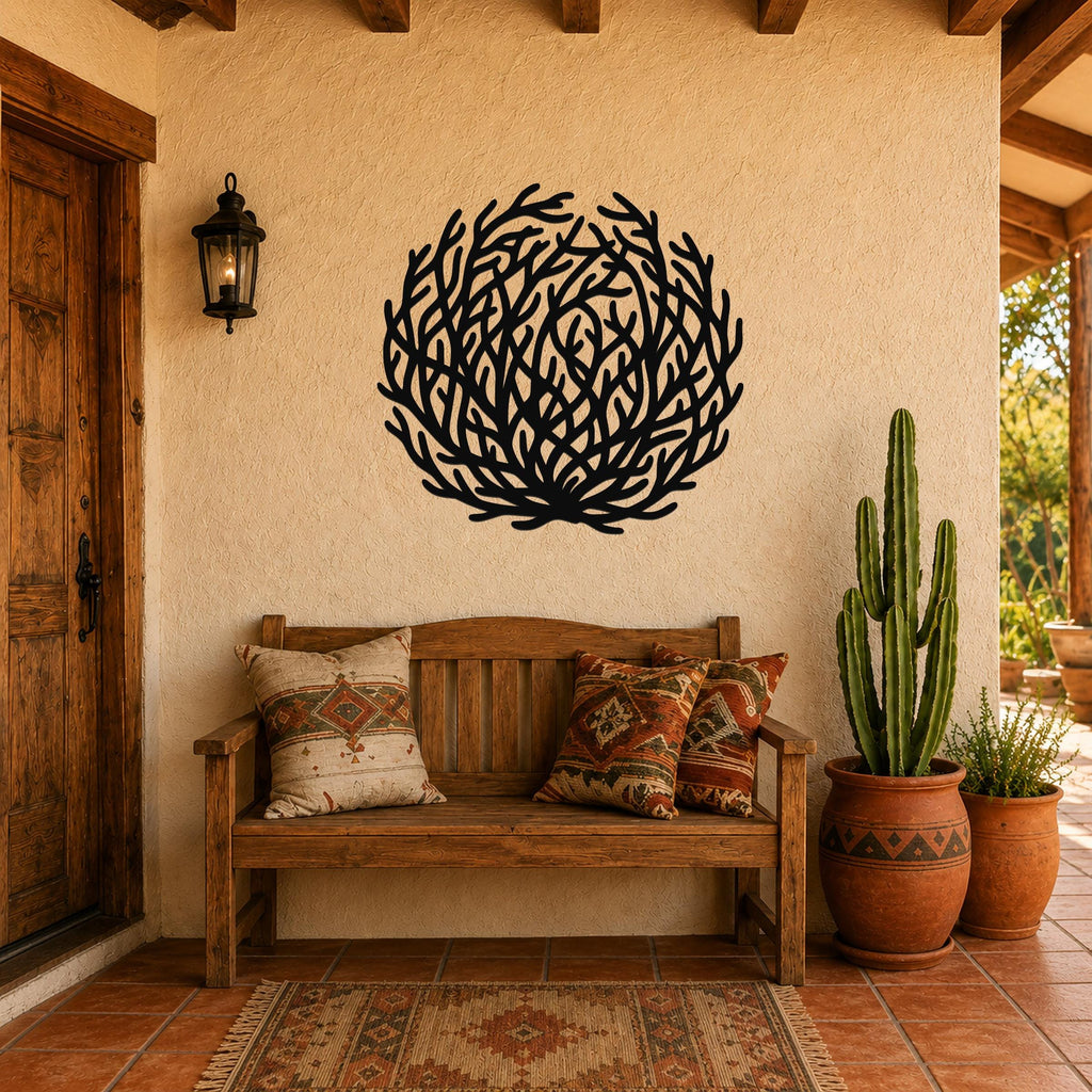 Black metal tumbleweed wall art with intricate branch cutouts, mounted on a stucco wall above a wooden bench in a rustic patio entryway.