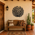 Black metal tumbleweed wall art with intricate branch cutouts, mounted on a stucco wall above a wooden bench in a rustic patio entryway.