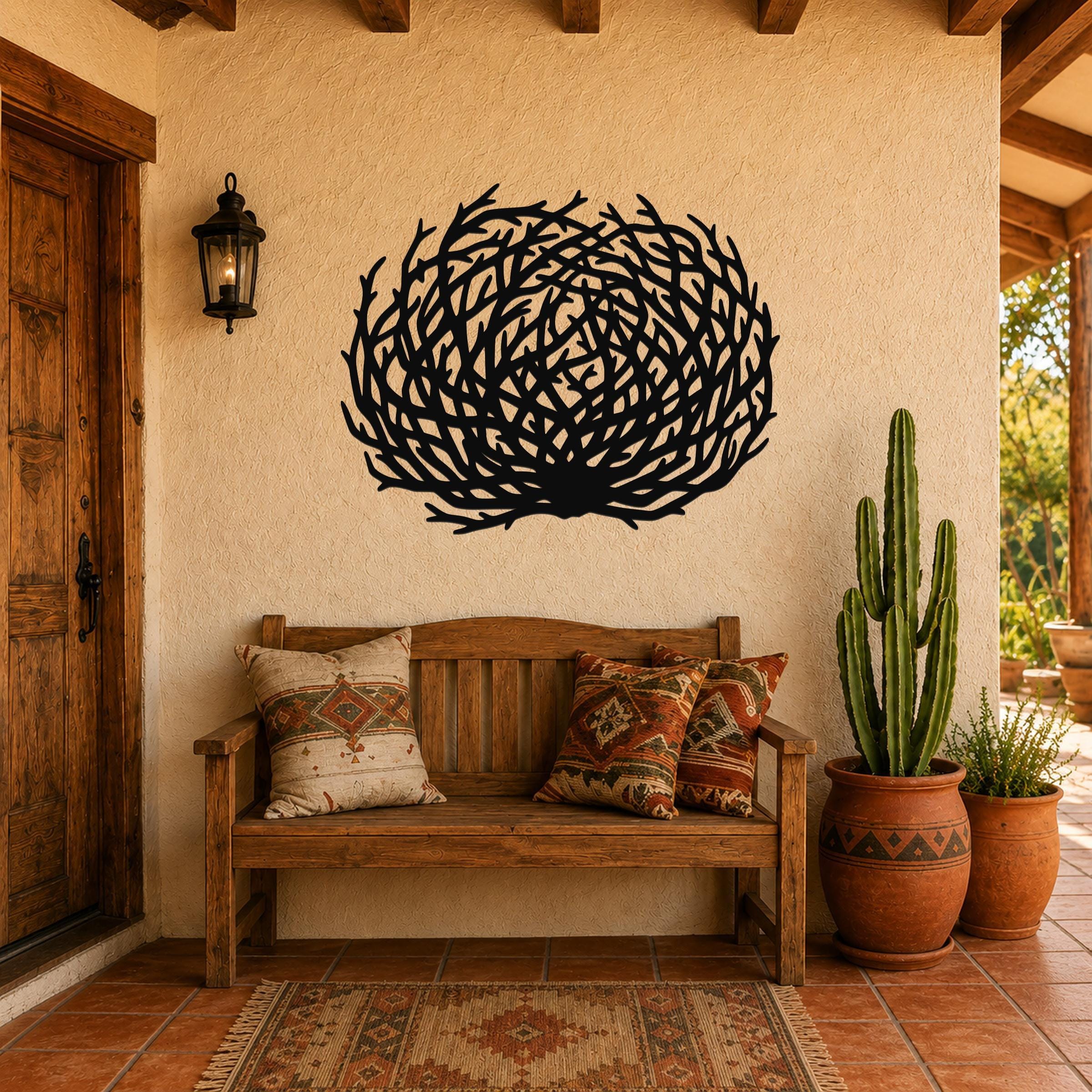 Black metal tumbleweed wall art with intricate branch cutouts, mounted on a stucco wall above a wooden bench in a southwestern-style patio entry.