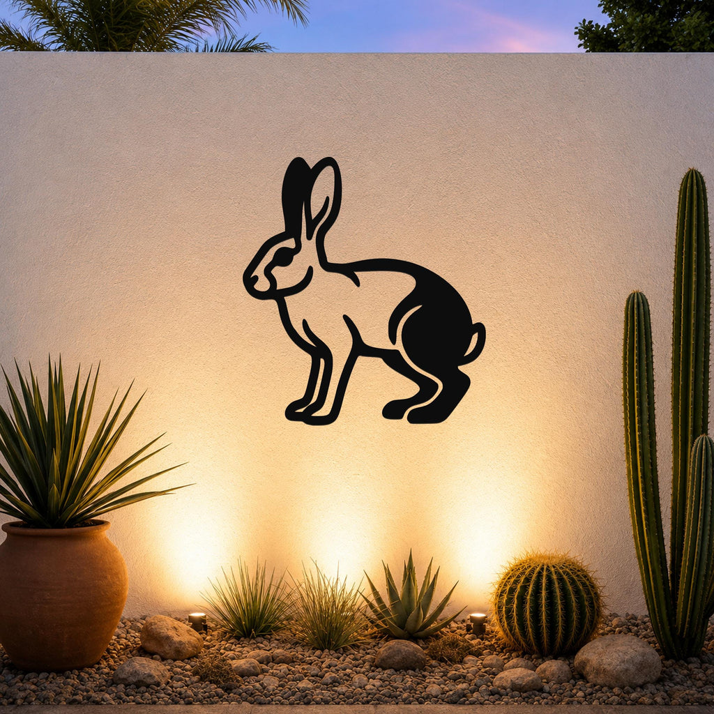 Black metal jackrabbit wall art silhouette mounted on a textured outdoor wall above a desert garden with cacti and warm uplighting.