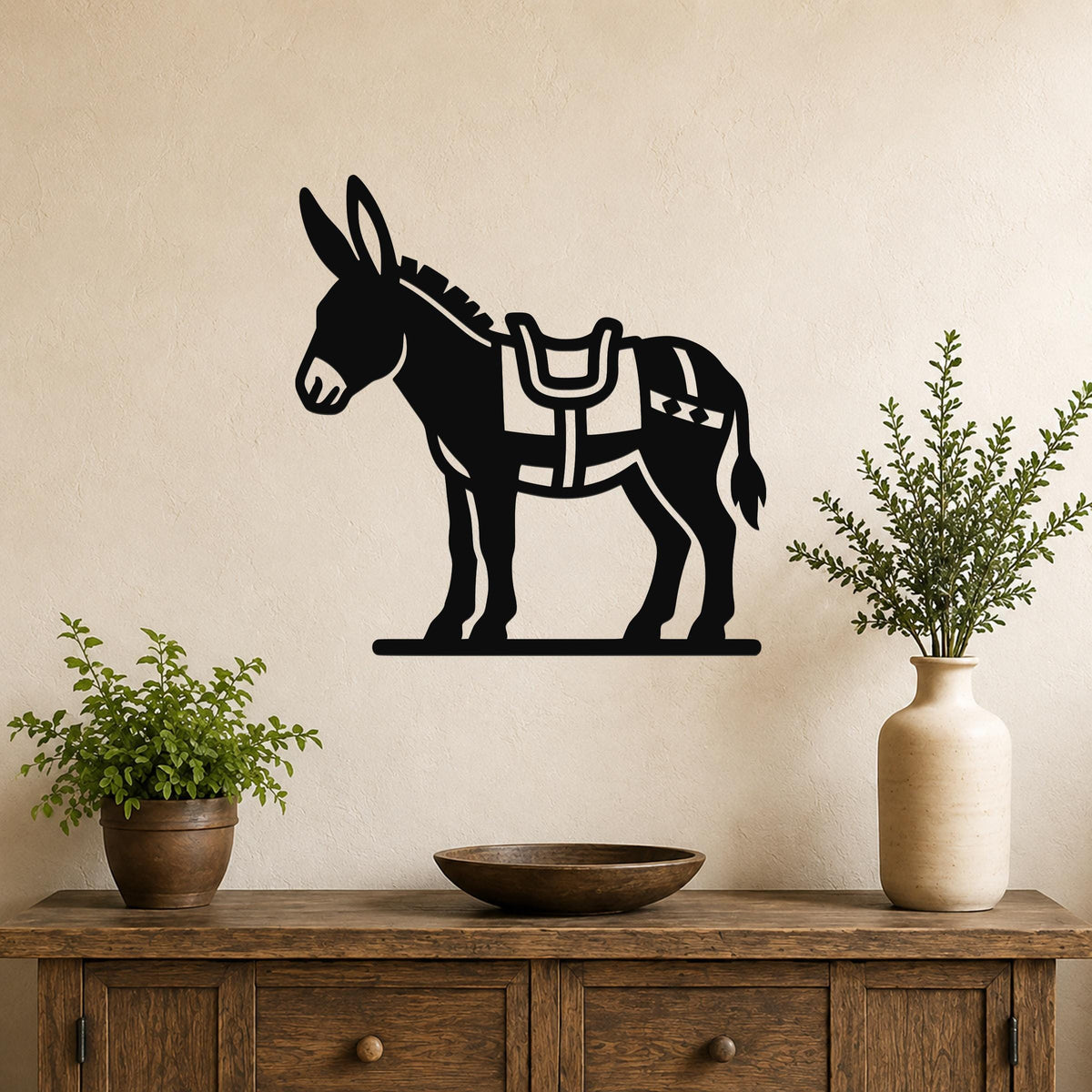 Black metal burro wall art with saddle and geometric cutouts, mounted on a beige wall above a wooden console table with potted plants.