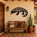 Black metal Gila monster wall art with geometric cutout patterns, mounted on a stucco wall above a wooden bench in a southwestern-style entryway.