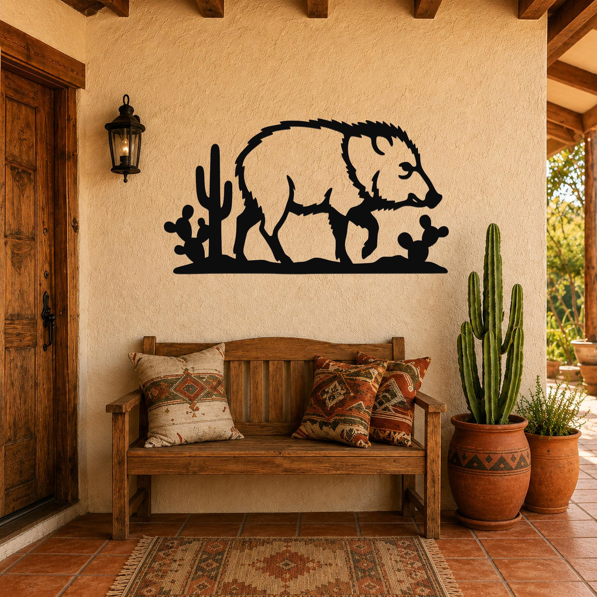 Black metal wall art silhouette of a javelina walking past cacti, mounted on a stucco wall above a wooden bench in a southwestern-style entryway.