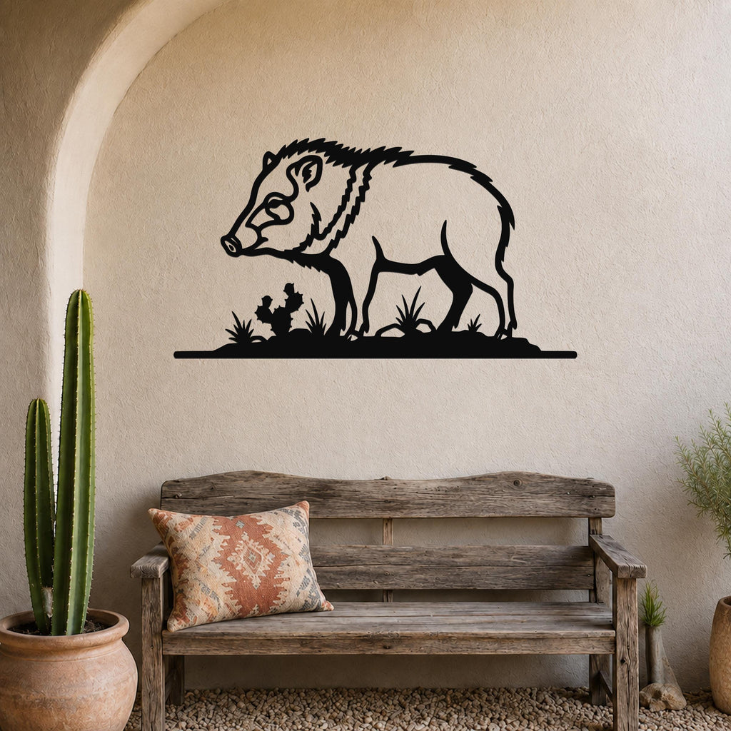 Black metal javelina wall art silhouette with cactus and grass cutouts, mounted on a stucco wall above a wooden bench in a southwestern-style entryway.
