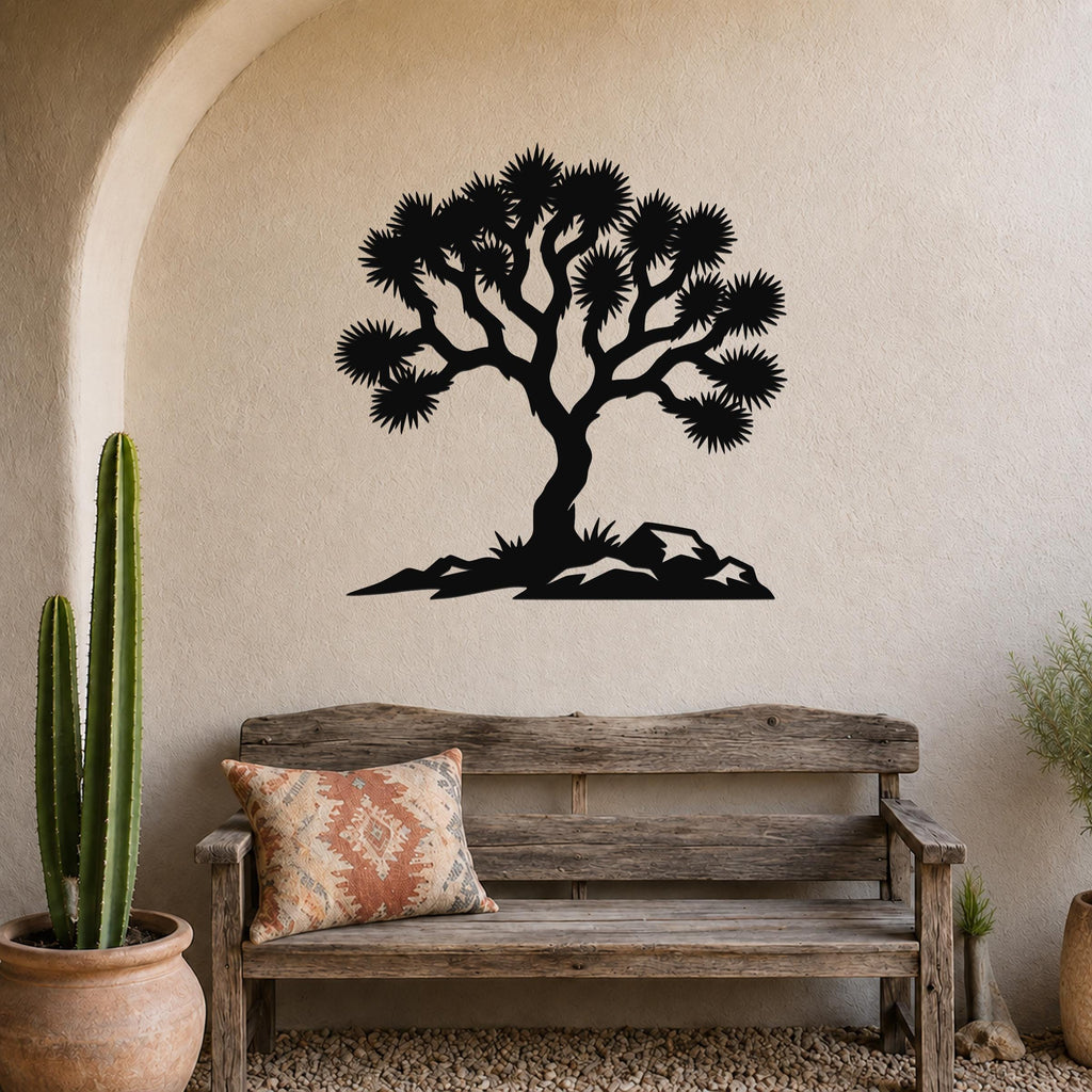 Black metal wall art silhouette of a Joshua tree with spiky branches and rocky base, mounted on a textured beige wall above a wooden bench in a southwestern-style living space.