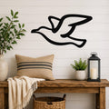 Black metal seagull wall art with motion-line cutouts, mounted above a wooden bench in a farmhouse-style entryway.